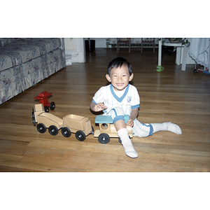 Young boy sits on the floor and plays with a wooden train toy