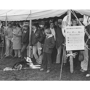 Observers stand under a tent at the Homecoming parade, including a husky