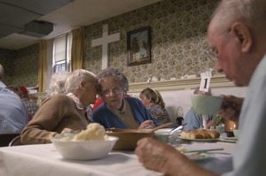 Church supper at the First Congregational Church, Whately: women seated at a table, whispering to one another, while eating supper