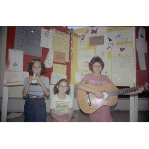 Three girls pose before a display of children's drawings.