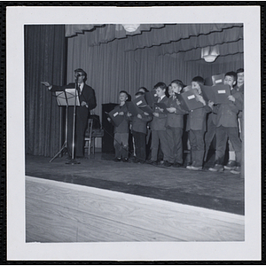 A man leads a boys' choir on stage during a Christmas party