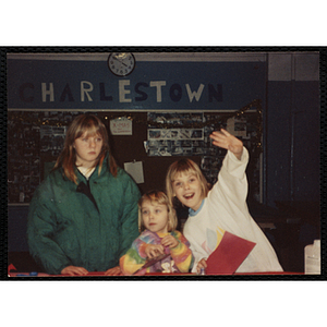 Three girls pose in front of a "Charlestown" bulletin board in the Charlestown Clubhouse