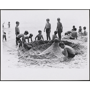 A group of boys build a sandcastle on the shoreline of a beach