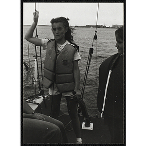 A girl holding a rudder stands on the deck of sailboat on Boston Harbor