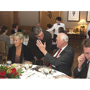 President Richard Freeland, bending down, talks with unidentified man at gala dinner for John Hatsopoulos