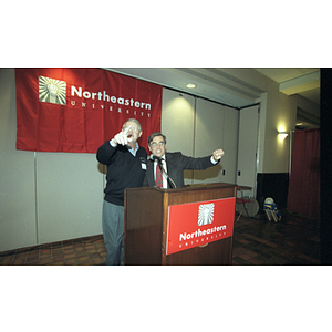 President Freeland and Chairman of the Board Neal Finnegan motion together at the podium at a reception