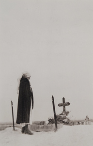 Red Cross worker standing in front of a grave marked with a cross and flowers