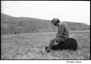 May Day at Packer Corners commune: man in a field, sitting on a guitar case