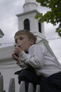 Church supper at the First Congregational Church, Whately: boy blowing on the seed head of a dandelion in front of the church