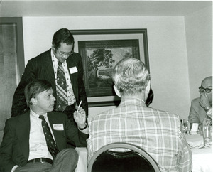 David C. Knapp seated at table at Alumni Board meeting holding cigarette with three unidentified men