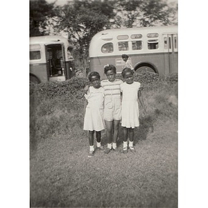 Three girls pose in front of buses after arriving at Breezy Meadows Camp