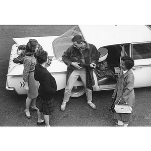 A student plays guitar next to a car as three others watch