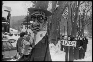 Bread and Puppet Theater protest against the invasion of Laos at the Vermont State Capitol, with large puppet and group of cloaked and masked figures carrying a sign reading 'Laos'
