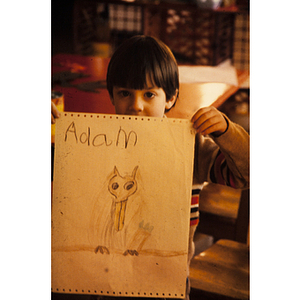 Boy holds up a hand drawn picture, signed "Adam"