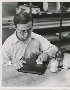 A man works on the wooden plaque for the 1951 president's trophy with linseed oil