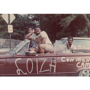 Three men sit in a car during a parade for the Festival Puertorriqueño