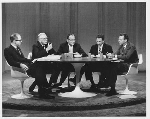 Louis M. Lyons sitting indoors, around a table, with group of men