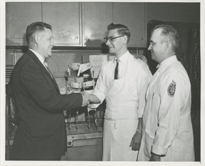 Willis C. Gorthy shakes hands with a technician in the Prosthetics and Orthotics lab while another man looks on