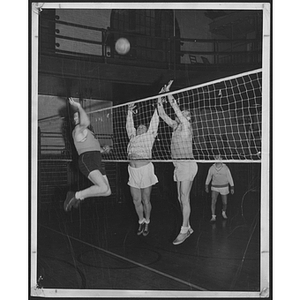 Three players jump in a game of volleyball