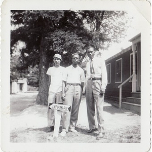 Three individuals pose behind a sign pointing to the infirmary at Breezy Meadows Camp
