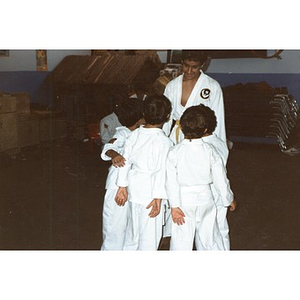 Four Latino boys are huddled around an older boy as they prepare to do a karate demonstration in a classroom at the Festival Betances, Boston, 1986.