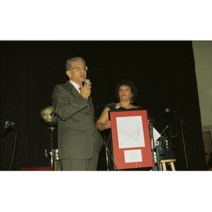 Man and woman on stage at Cultura Viva with framed drawing of Taino Tower.