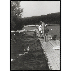 A swimming supervisor stands on the dock watching a group of children