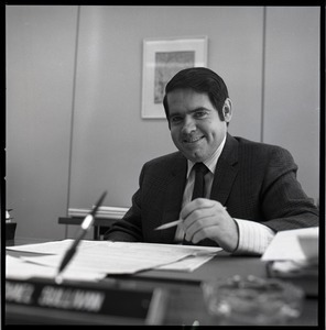 Michael Sullivan seated at his desk, pen in hand: Treasurer's Office, University of Massachusetts