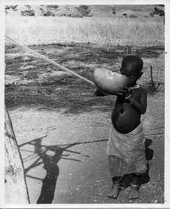 Kirdi child drinking from a gourd, clad only in a discarded plastic wrapper