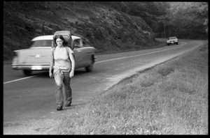 Backpacker walking along a highway, cars speeding past