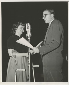 A woman using forearm crutches and an unidentified man stand next to an American Broadcasting Company microphone