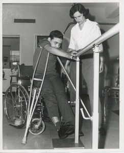 Luis Damilano using parallel bars with assistance from a physical therapist