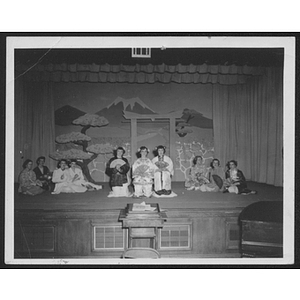 Actors sit on a stage, wearing costumes meant to imitate traditional East Asian clothes
