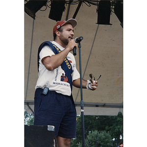 A man wearing a sash speaks into a microphone on stage at the Festival Puertorriqueño