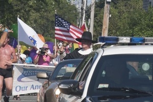 Police escort leading the approaching parade, with man dressed in Puritan costume ringing a bell : Provincetown Carnival parade