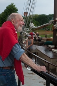 Pete Seeger: three-quarter length portrait on the docks, looking over a boat at the Clearwater Festival