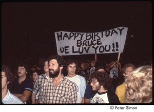 MUSE concert and rally: men in the MUSE concert audience, sign in background reads, 'Happy Birthday Bruce, We Luv You!'