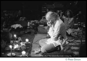 Ram Dass seated onstage at the Winterland Ballroom during his 'marathon,' head bowed