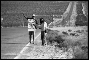 Activists standing by the road near entrance to the Nevada Test Site holding a sign reading 'Stop testing now,' at the Nevada Test Site peace encampment