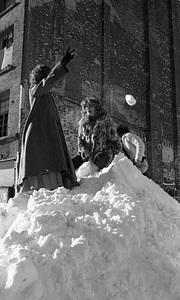 Three women throwing snowballs atop large snowpile