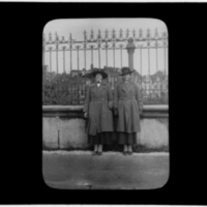 Two women on a bridge in front of damaged buildings