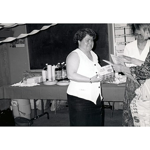 Laura Buxbaum and Clara Garcia hand a certificate and a box of Play-Doh to a woman during a Child Care Program training and celebration.
