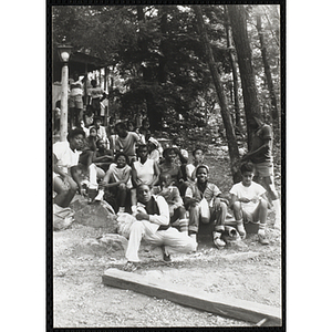 A group of youth sit on a hill by a building in the woods