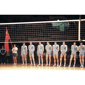 Members of the Men's Chinese Volleyball Team stand in a line behind a volleyball net, while a woman at the end of the line holds a Chinese flag