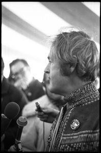 Timothy Leary surrounded by press and supporters, drinking from a paper cup