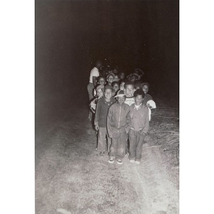A group of young boys walks down a dirt road at night
