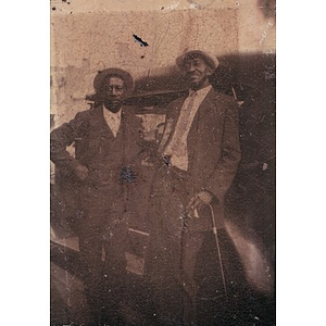 Two African American men leaning against car