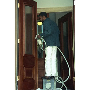 Workman using an airbrush to paint the front doors of Residencia Betances.