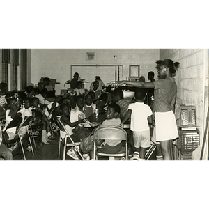 Roxbury Boys and Girls Club members sit around tables with flowers in their hands while a girl stands pointing at something