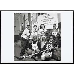 Seven Boys and Girls Club members pose in front of the Club banner in a gymnasium, wearing uniforms of four major sports teams in Boston: Bruins, Celtics, Red Sox, and New England Patriots